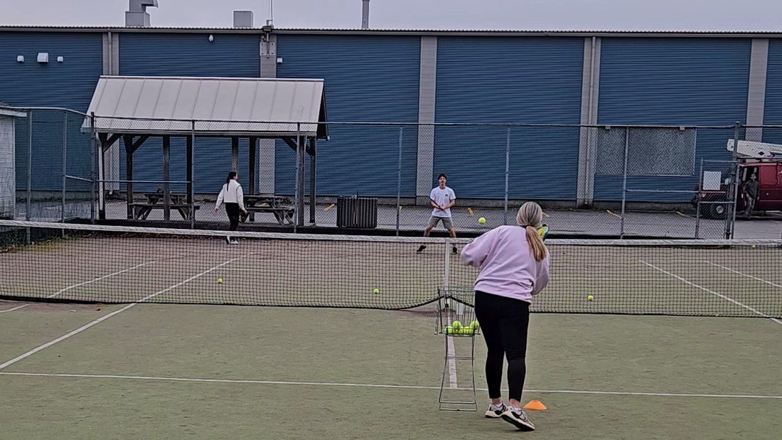 Aleksandra Wozniak feeding balls to a young player on a court at her tennis academy in Bedford